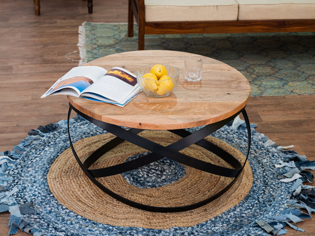 Table à café ronde en manguier sur base d'anneaux en métal noir, sur un tapis rond