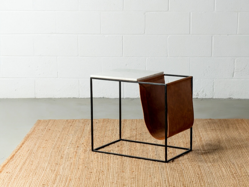 Table Masika contre un mur blanc, porte-revues en similicuir brun