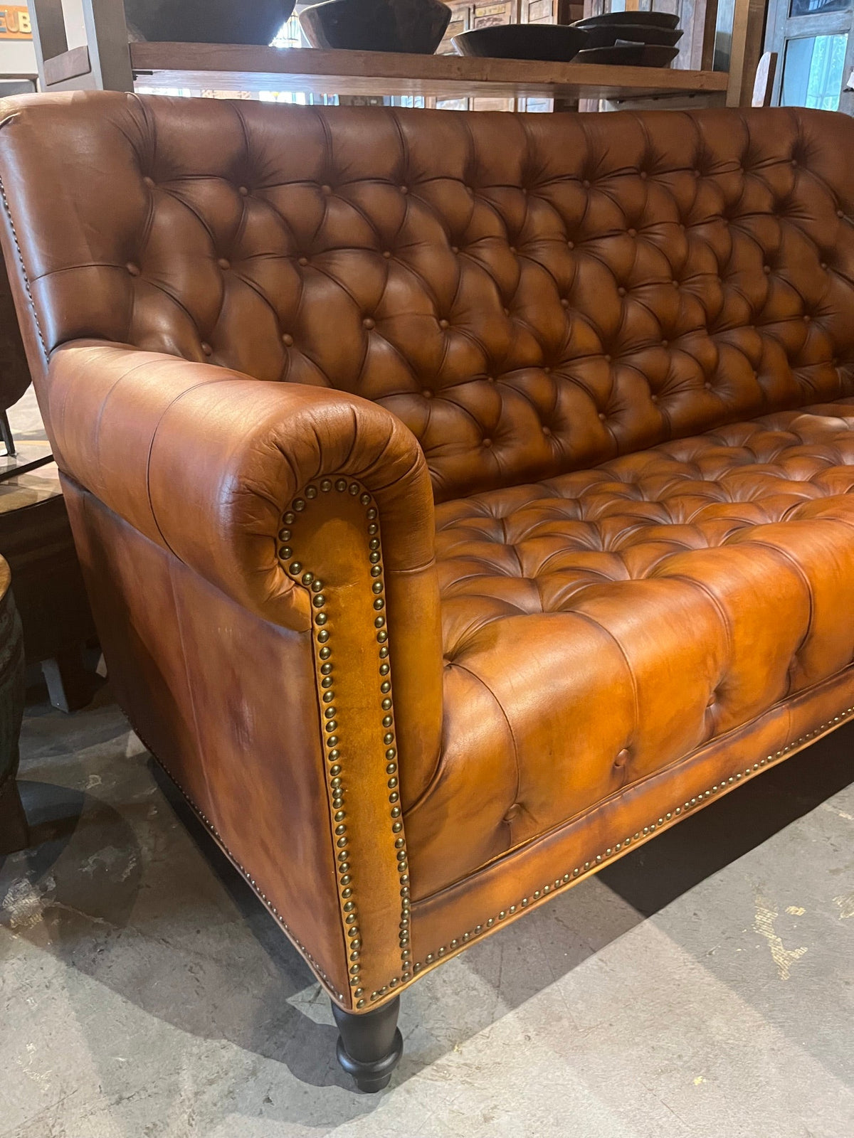 Accoudoir roulé bordé de clous décoratifs sur un canapé Chesterfield en cuir cognac