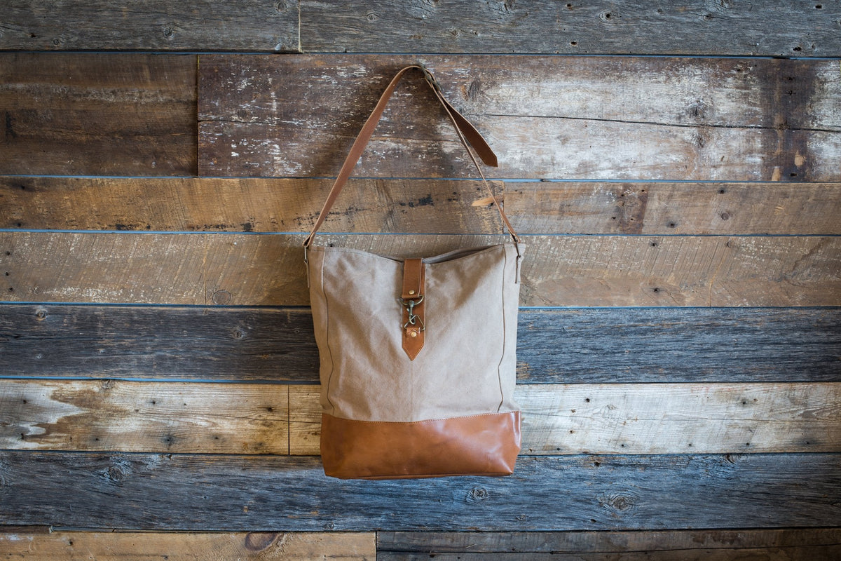Sacoche en toile beige à fond de cuir, suspendue par sa bandoulière